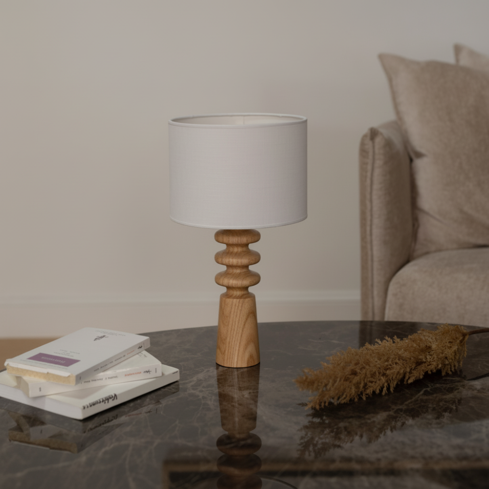 Verschönern Sie Ihren Wohnraum mit dieser eleganten Tischleuchte aus Holz mit einem skulpturalen Sockel und einem klassischen Lampenschirm aus Stoff. Die warmen Holztöne in Kombination mit dem minimalistischen Design machen sie zu einer vielseitigen Ergänzung für jedes Interieur, von modern bis rustikal. Diese Lampe eignet sich perfekt für Nachttische, Wohnzimmer oder Heimbüros und sorgt für ein sanftes Umgebungslicht, das eine gemütliche Atmosphäre schafft. Der handgefertigte Holzsockel verleiht ihr einen 