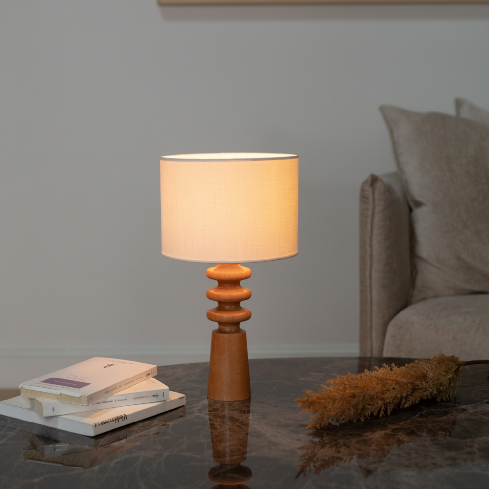 Verschönern Sie Ihren Wohnraum mit dieser eleganten Tischleuchte aus Holz mit einem skulpturalen Sockel und einem klassischen Lampenschirm aus Stoff. Die warmen Holztöne in Kombination mit dem minimalistischen Design machen sie zu einer vielseitigen Ergänzung für jedes Interieur, von modern bis rustikal. Diese Lampe eignet sich perfekt für Nachttische, Wohnzimmer oder Heimbüros und sorgt für ein sanftes Umgebungslicht, das eine gemütliche Atmosphäre schafft. Der handgefertigte Holzsockel verleiht ihr einen 